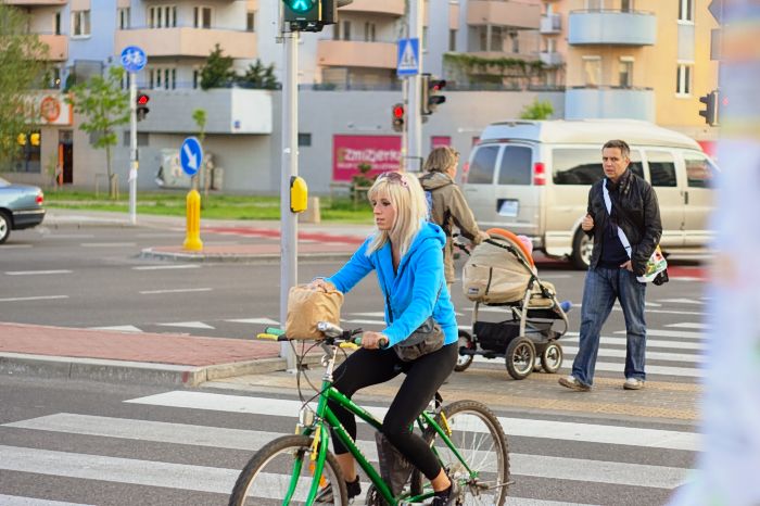 Huebsche Frau auf gruenem Fahrrad ueberquert Zebrastreifen wobei sie ihre Einkaufstuete auf dem Lenker feshaelt